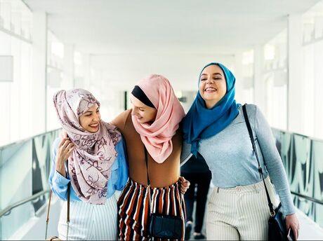 Three young women, wearing beautiful hijabs, hugging each other and laughing in a hallway
